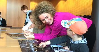 Am Besprechungstisch in der Runde: Kleiner Junge zeigt Iris Kühnberger sein Foto